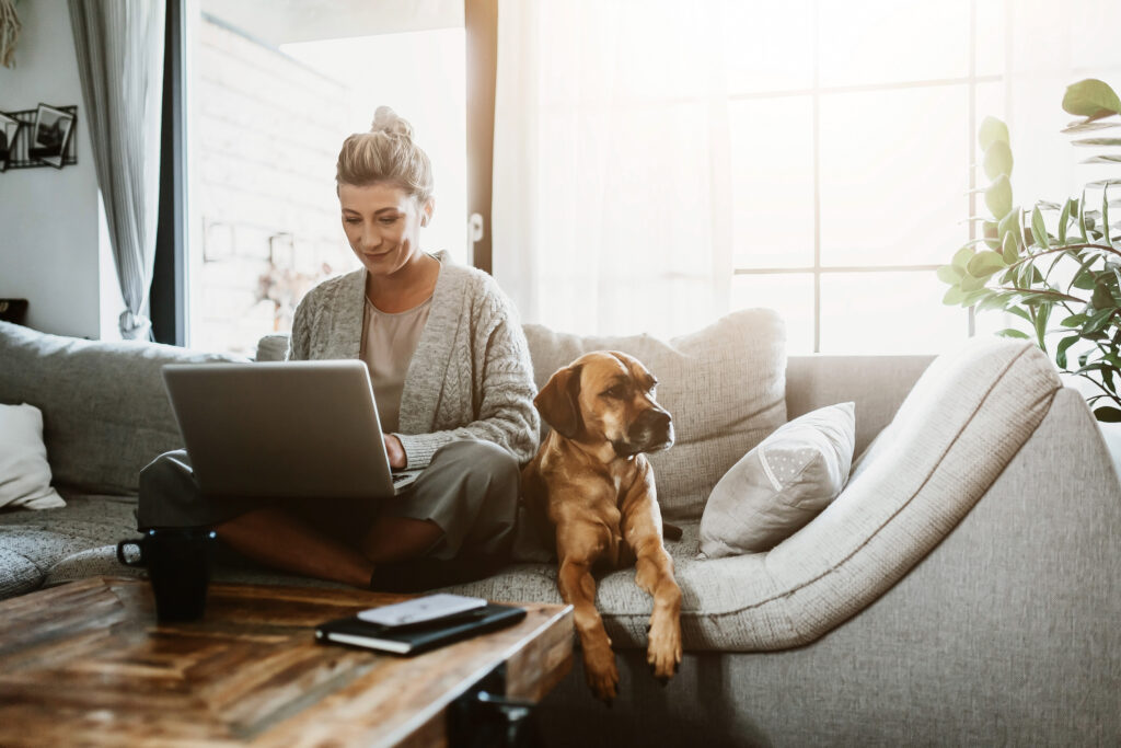 Mujer trabajando en su laptop desde casa junto a su perro mientras organiza su presupuesto financiero.