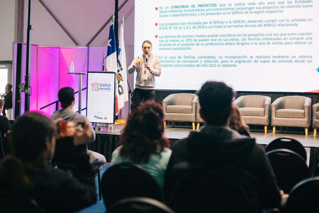 Persona exponiendo sobre proyectos habitacionales en Expo Vivienda 2025 ante un público atento, con pantalla informativa de fondo.